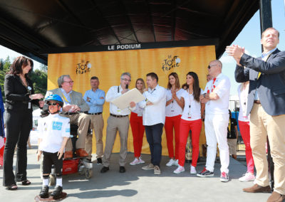 Sous les yeux de Muriel Targnion, bourgmestre de Verviers, Christophe Penot, l’organisateur, présente au lauréat, Stéphane Thirion, le portfolio du 13e Prix Jacques-Goddet frappé aux couleurs du Tour de France et de Carrefour. Une autre façon de saluer tous ceux qui concourent, d’année en année, au rayonnement du Prix Jacques-Goddet.