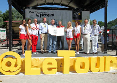 Photographie officielle de la remise du 12e Prix Jacques-Goddet à Moirans-en-Montagne, sous les couleurs habituelles du maillot blanc à pois rouges. François Thomazeau, le lauréat, a reçu son trophée des mains de Christian Prudhomme, le directeur du Tour de France, accompagné d'Éric Marchyllie, responsable sponsoring de Carrefour France, et Frédéric Ebling, directeur des affaires publiques du groupe Carrefour France.