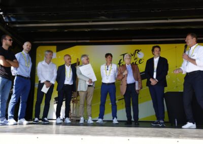 Au côté de Thomas Perotto, le lauréat, premier sur la gauche, les jurés du 21e Prix Jacques-Goddet – Trophée Amaury Sport Organisation, ont pris place sur le podium du Village du Tour de France, le 11 juillet 2025, à Saint-Malo, au départ de la septième étape. On peut reconnaître Jean-Étienne Amaury, Sébastien Grosmaitre, Xavier Jan, Christophe Penot, Julien Goupil, Jean-Claude Trichet, Laurent-Éric Le Lay et Christian Prudhomme, directeur du Tour de France, qui rappelle que la course cycliste et la presse écrite, historiquement, ont toujours fait cause commune.