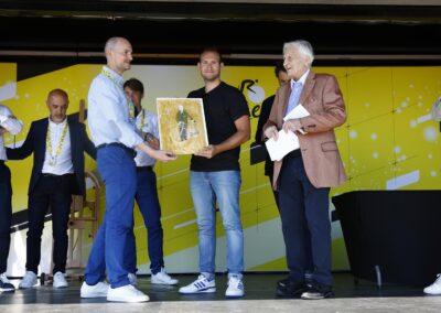 Jean-Étienne Amaury, président du groupe éponyme, et Jean-Claude Trichet, président du 21e jury, remettent à Thomas Perotto le tirage sur papier unique, spécialement réservé au lauréat. Un Jacques Goddet hardiment portraituré, le vélo à la main, par le peintre français Frédéric Brandon, formé jadis aux beaux-arts de Paris et candidat, en 1968, au Prix de Rome !