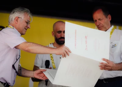 L’instant solennel. Christophe Penot et Christian Prudhomme présentent à Quentin Girard la preuve de sa gloire : un tirage unique de l’œuvre d’Olivier Masmonteil, spécialement réalisé sur papier Artistica.